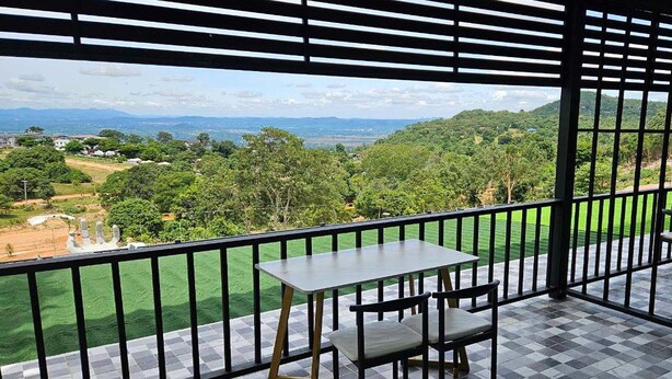 Een balkon met een tafel en stoelen, met uitzicht op een groen landschap en verre bergen.