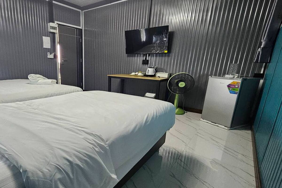 A hotel room with two beds, a TV, a desk with a fan, and a refrigerator.