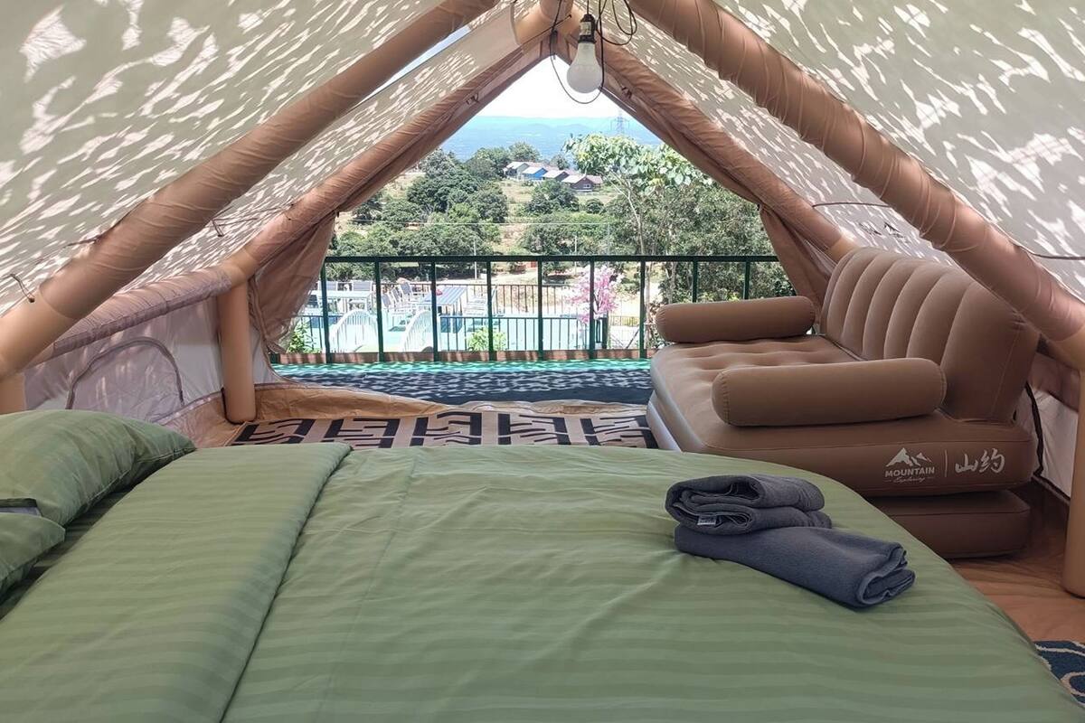 A cozy tented accommodation with a bed, a cushioned seating area, and a view of the outdoors.