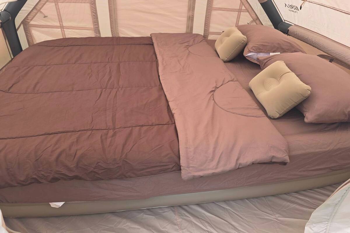 A bed with a brown bedspread and beige pillows in a tent-like room.