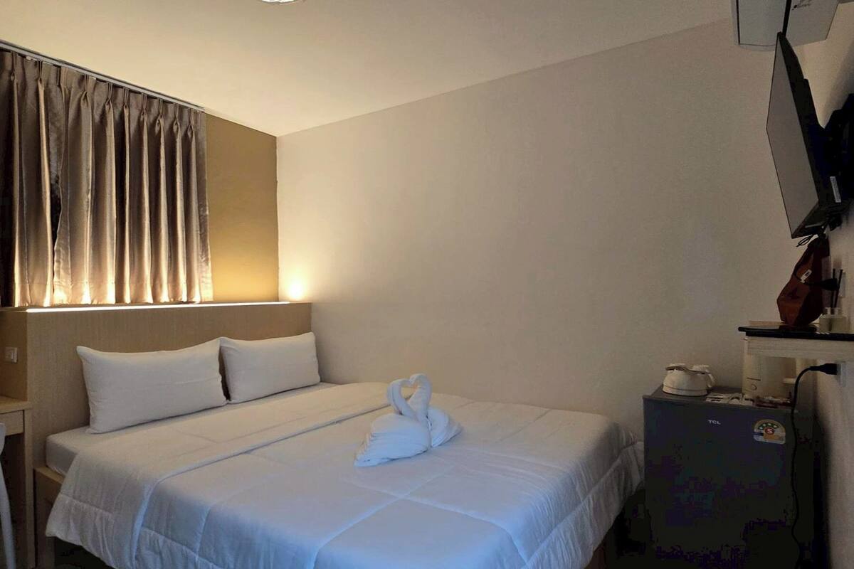 A hotel room with a neatly made bed, a flat-screen TV, and a small table with a kettle.