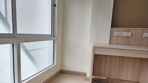 A corner room with a large window, a wooden desk, and a wall-mounted electrical outlet. - Reezq Hostel (Bangkok)
