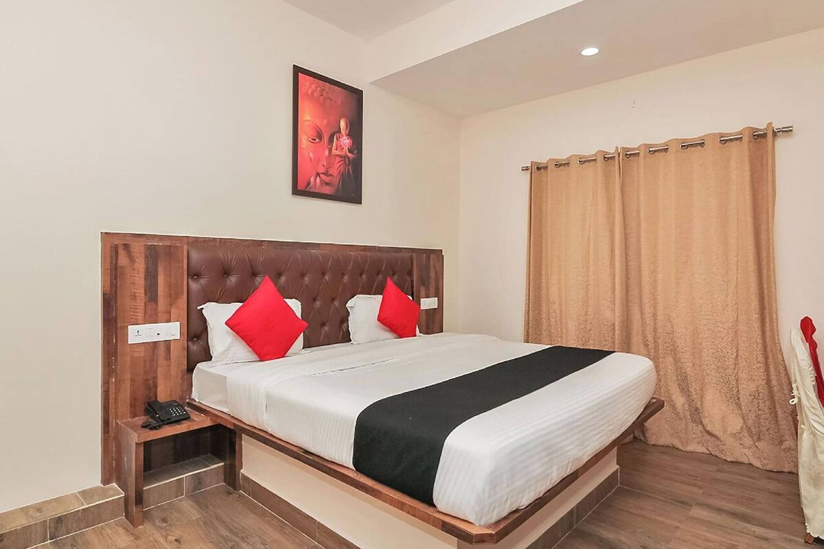 Ein Hotelzimmer mit einem großen Bett, einem Holzkopfstück, einem Nachttisch mit Telefon und einem Vorhang.