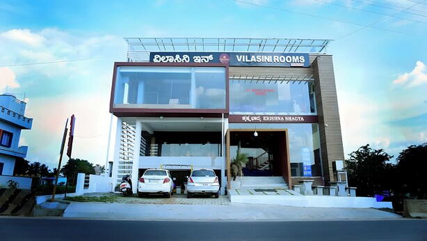A two-story building with a sign for 'Vilasini Rooms' and 'Krishna Bhagya'.