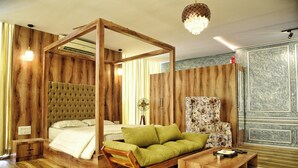 A room with a four-poster bed, a green sofa, a wooden coffee table, and a floral armchair.