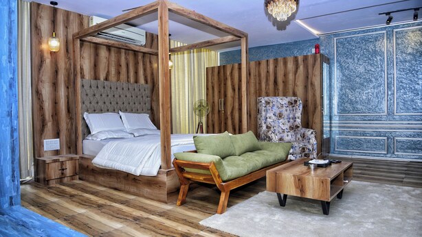 A room with a wooden four-poster bed, a green sofa, a wooden coffee table, and a patterned armchair. - Vilasini Inn (Madduru)