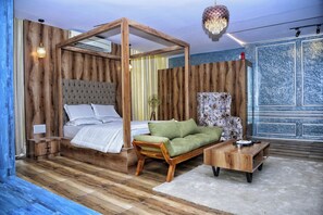 A room with a wooden four-poster bed, a green sofa, a wooden coffee table, and a patterned armchair.