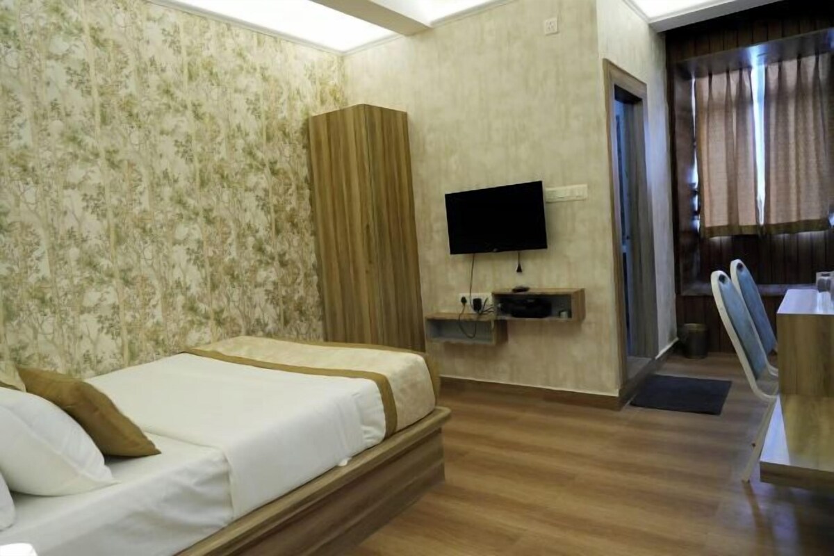 Una habitación de hotel con cama, televisión, un escritorio pequeño y zona de ducha.