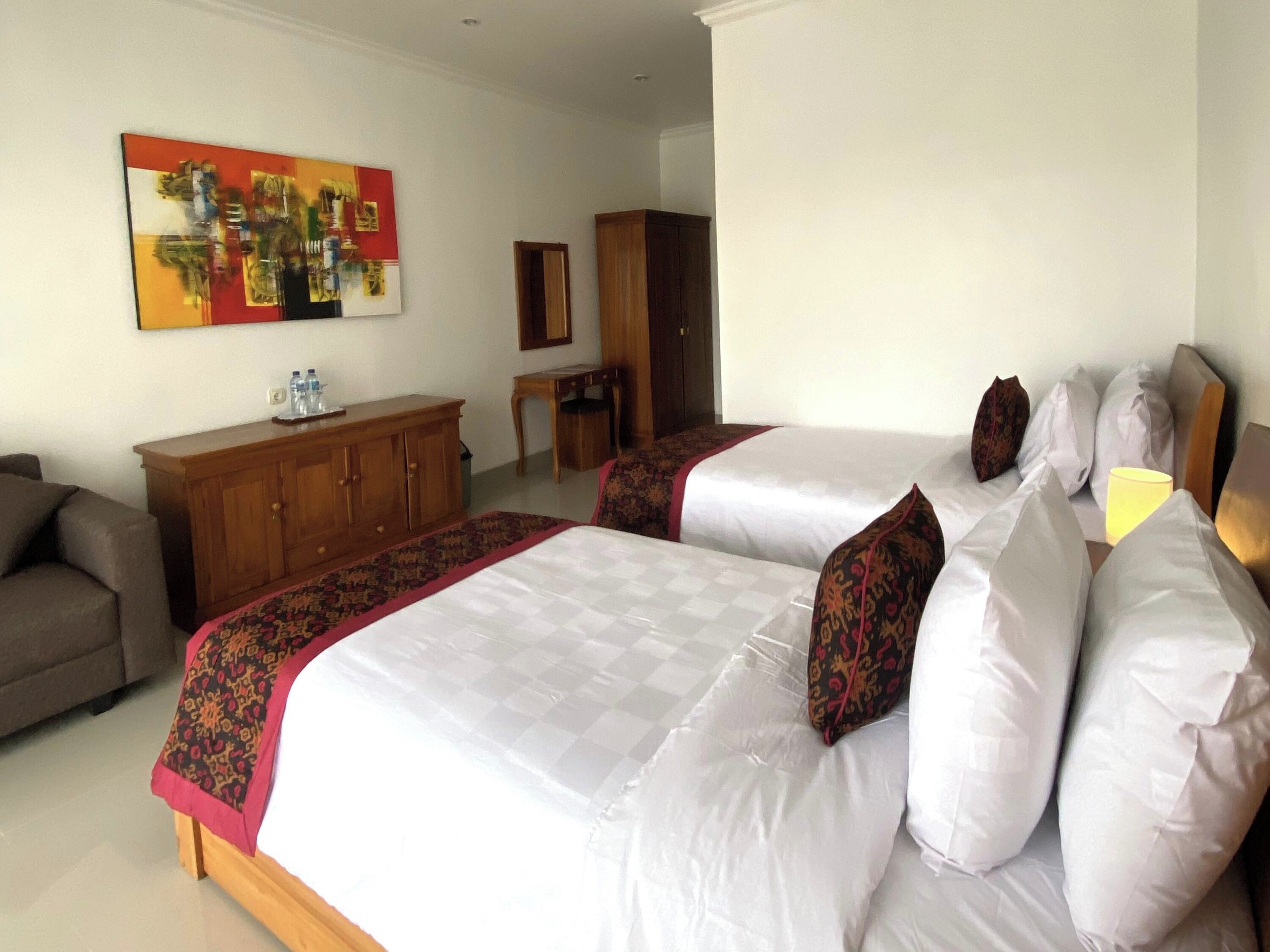 Une chambre d’hôtel avec deux lits, une commode en bois, un bureau et un tableau au mur.