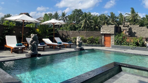 A pool area with lounge chairs and umbrellas, surrounded by tropical plants and a stone wall. - Nivaluma By Zuzu (Mas)