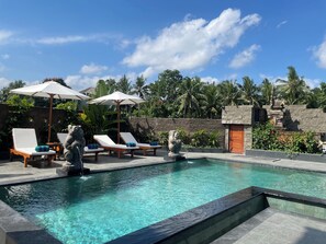 A pool area with lounge chairs and umbrellas, surrounded by tropical plants and a stone wall. - Nivaluma By Zuzu (Mas)