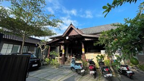 A traditional building with a tiled roof and a covered entrance. There are several parked scooters and a car in front of the building. - Nivaluma By Zuzu (Mas)