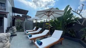 A poolside area with lounge chairs and umbrellas, surrounded by tropical plants and a stone statue. - Nivaluma By Zuzu (Mas)