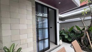 A modern building with a large sliding glass door, a tiled exterior wall, and a balcony with wicker furniture and potted plants. - Ranala Coliving (Keroboken Kelod)