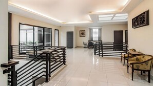 A spacious hotel lobby with a high ceiling, modern lighting, a staircase, and a seating area with chairs and a table. - TOS Guest House By Zuzu (Jakarta)