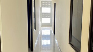 A corridor with a tiled floor leading to a bright room with a large window. - TOS Guest House By Zuzu (Jakarta)