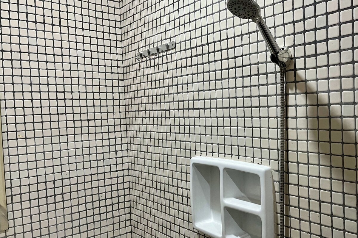 A tiled shower area with a handheld showerhead and a white soap dispenser.