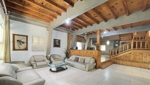 A spacious living room with a high wooden ceiling, a sofa set, a glass coffee table, and a staircase leading to an upper level. - Villa 325 By Zuzu (Lembang)
