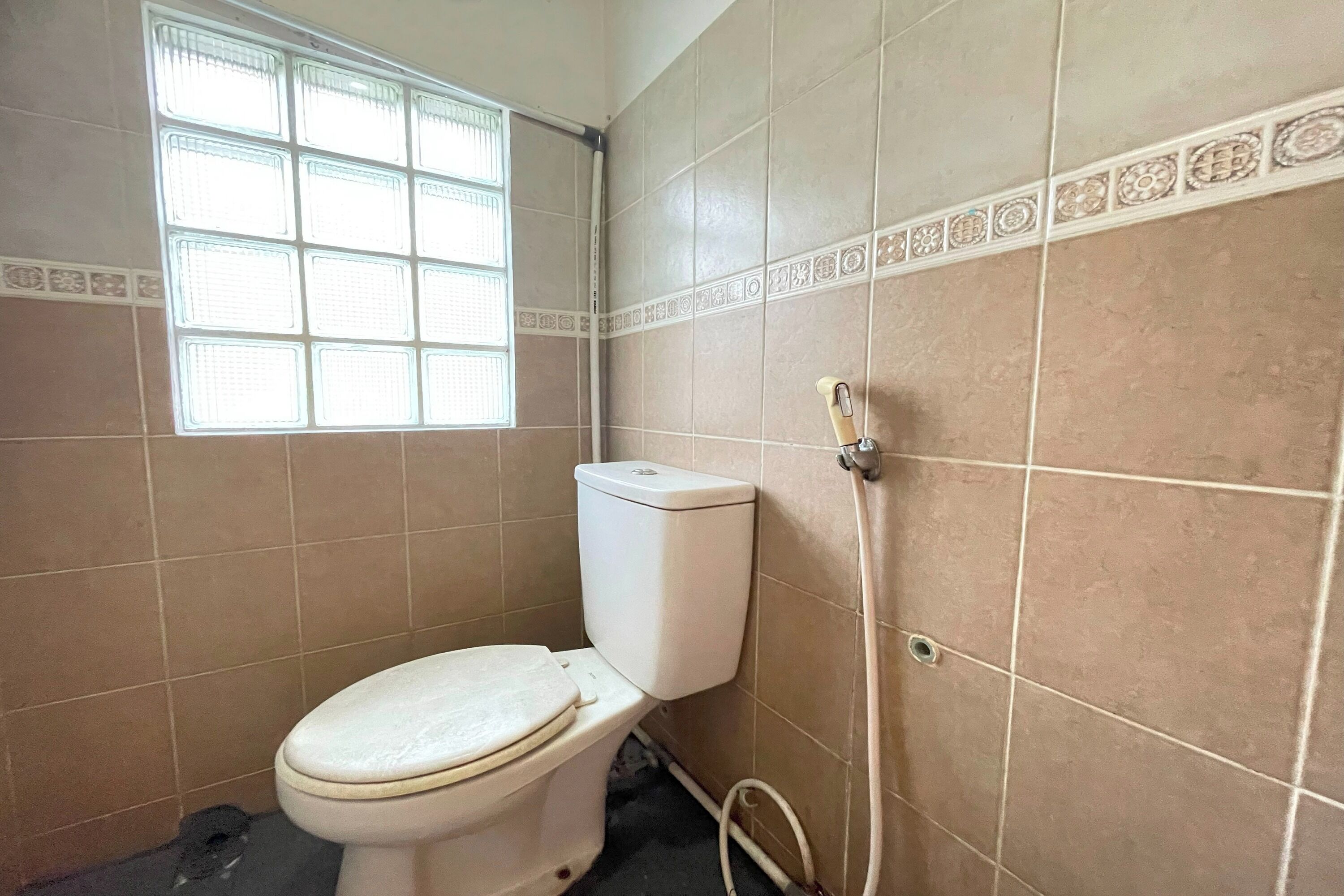 Ein Badezimmer mit Toilette, Fenster und Fliesenwänden.