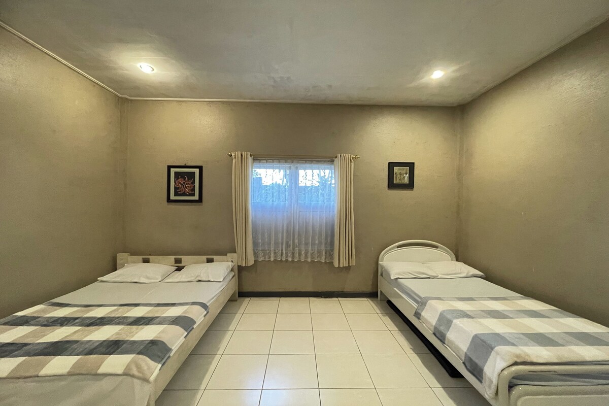 A small, clean room with two single beds, a window with curtains, and a ceiling light.