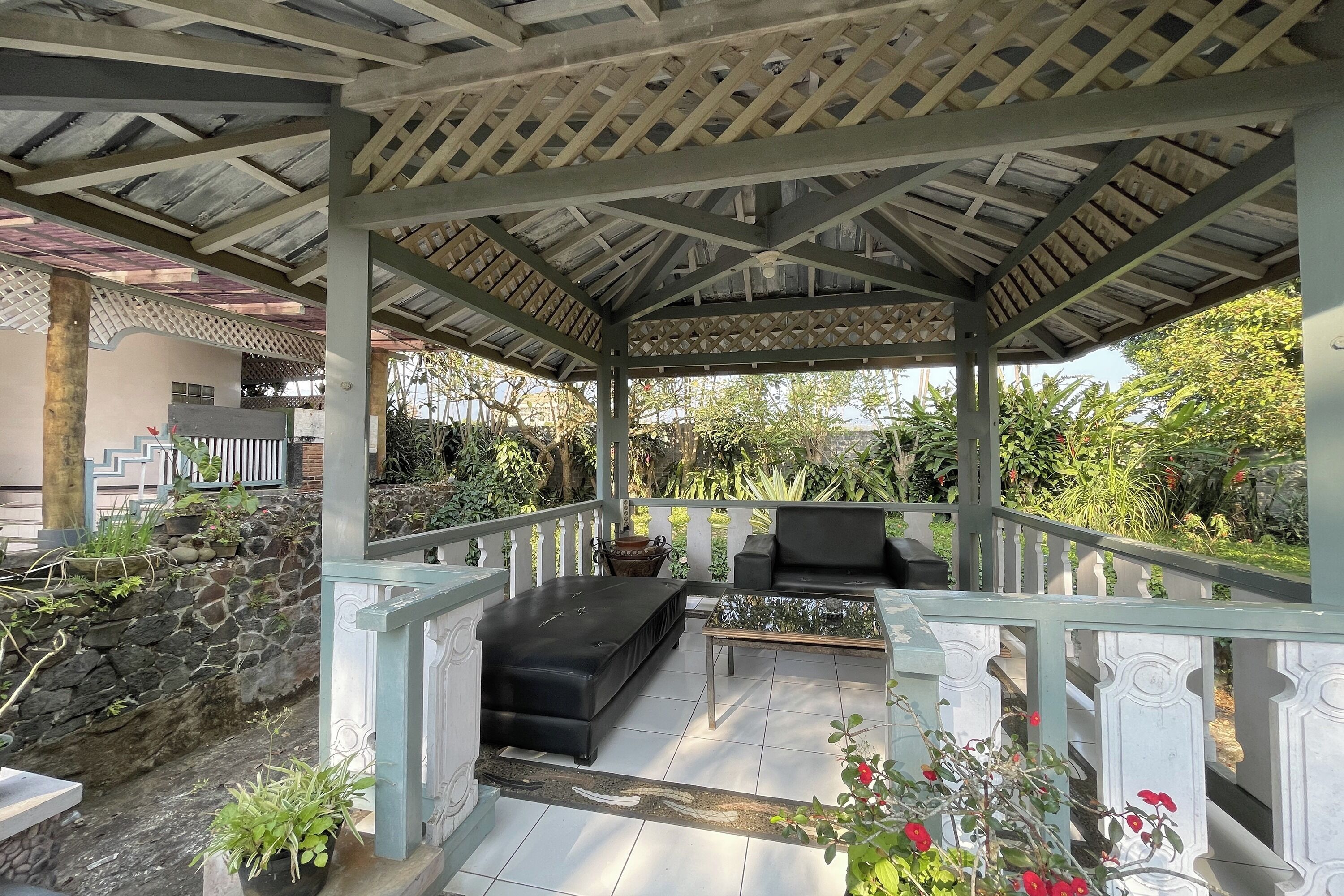 Uma área de varanda coberta com parede de pedra, um sofá preto e uma mesa.