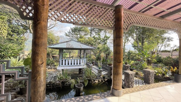 A covered garden area with a small pond, a wooden gazebo, and stone steps leading to a bridge. - Villa 325 By Zuzu (Lembang)
