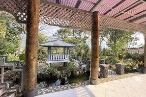 A covered garden area with a small pond, a wooden gazebo, and stone steps leading to a bridge. - Villa 325 By Zuzu (Lembang)