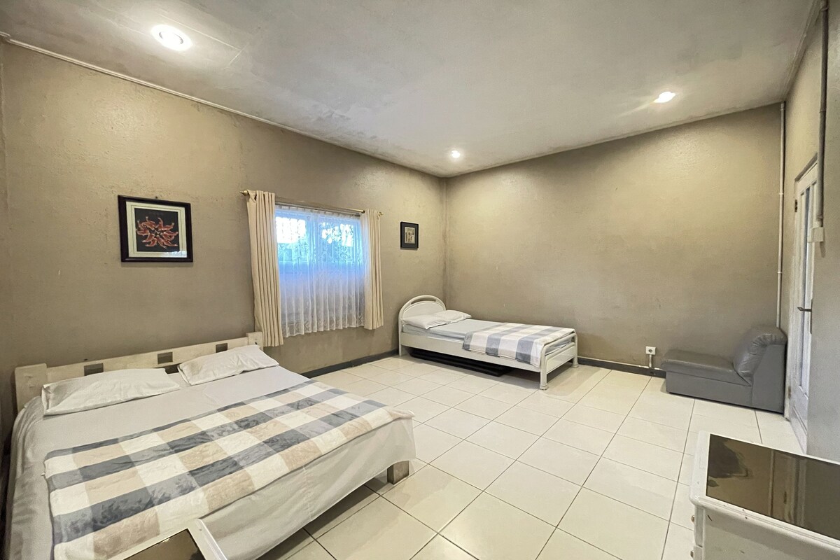 A bedroom with two beds, a window with curtains, and a small sofa.