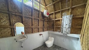 A bathroom with a toilet, sink, and shower. The walls are made of woven bamboo, and the floor has a patterned tile design.