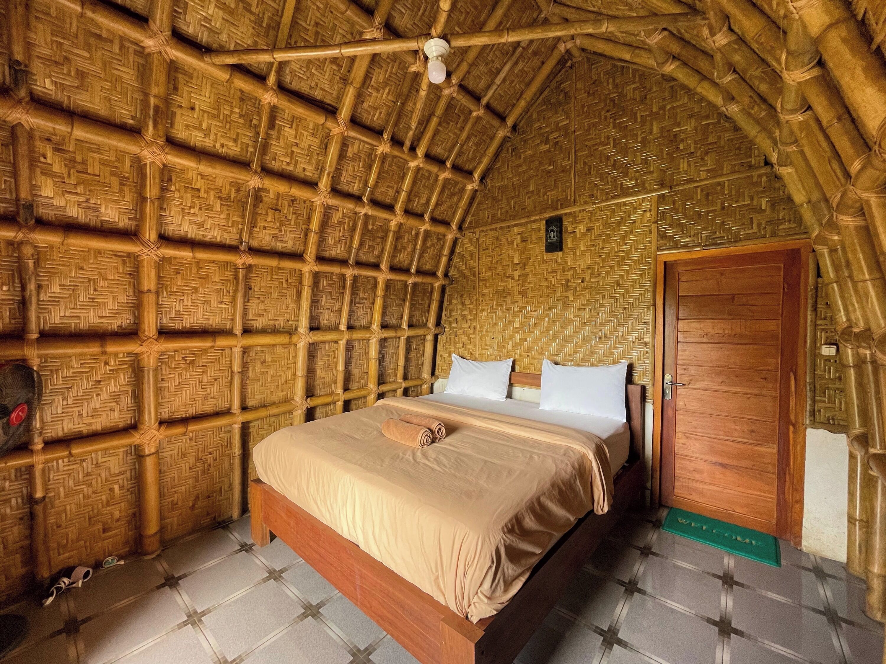 Una habitación con techo de paja, una cama de madera y una puerta de madera.