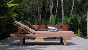 En liggestol med markise, placeret på en terrasse med udsigt til frodig vegetation.