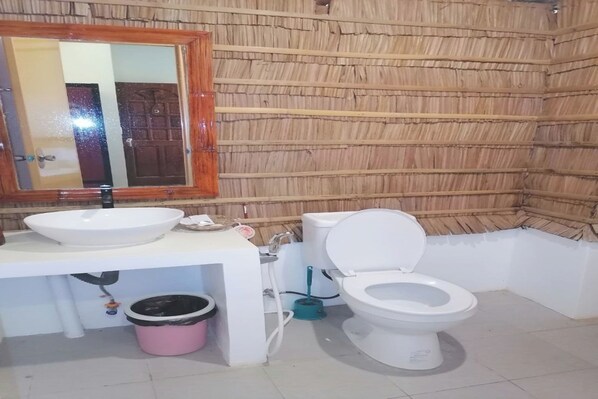 A bathroom with a wooden wall, a white sink, a toilet, and a mirror with a wooden frame. - Avila's Hostel Moalboal near Beach (Moalboal)