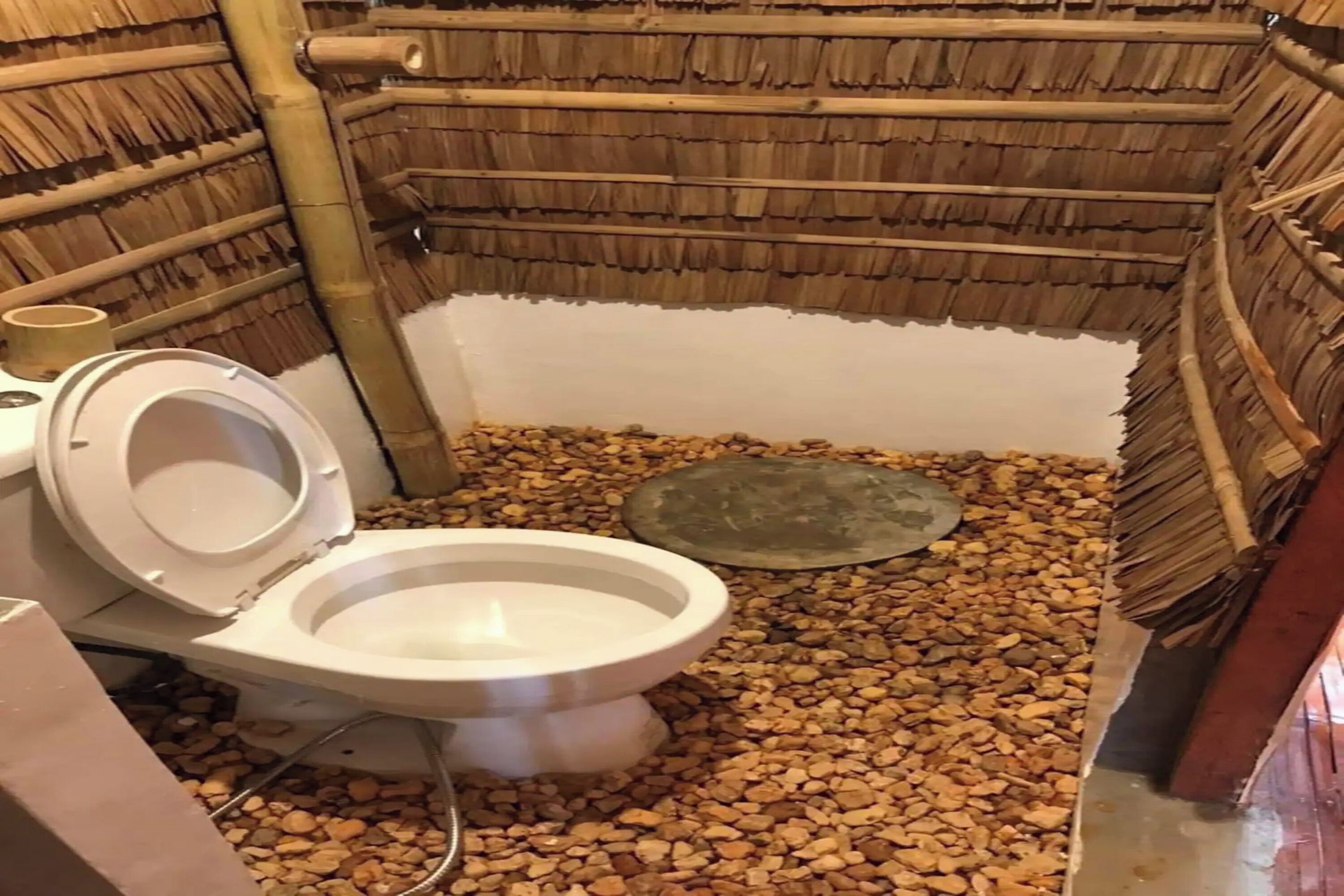 Un baño con techo de bambú, inodoro y suelo de guijarros.