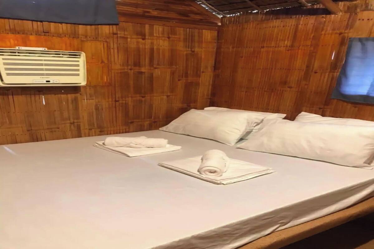 Ein Zimmer mit Holzwänden, einem Bett, weißen Leinen und einer Wand-Klimaanlage.