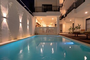 Piscina con cubierta de madera y sillas reclinables, balcón con barandilla y área de cocina visible a través de una separación.