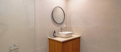 A modern bathroom with a wooden vanity, a round mirror, and a white sink.