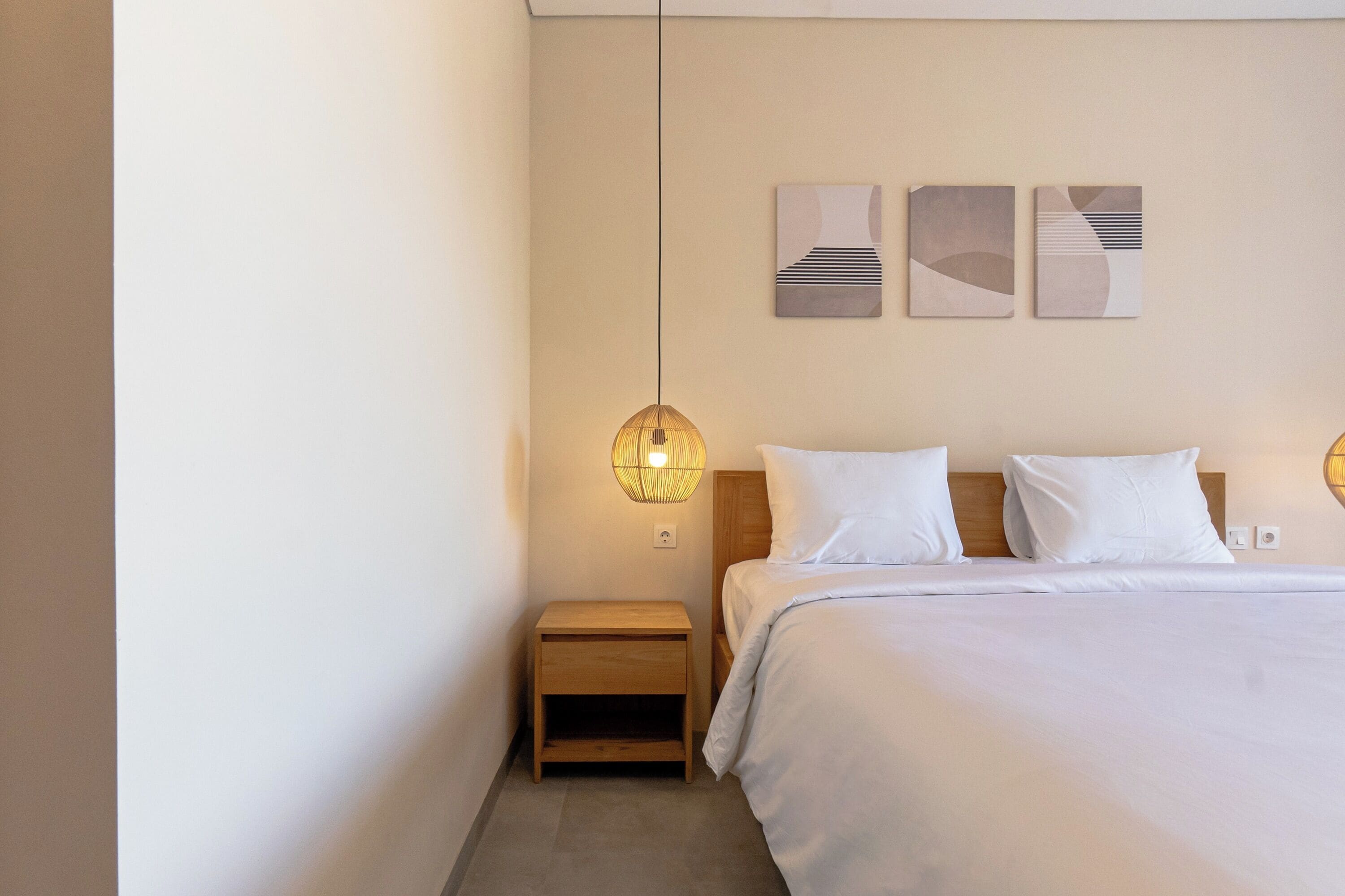 Un dormitorio con cama, mesita de noche, lámpara de pared y obras de arte abstracto.