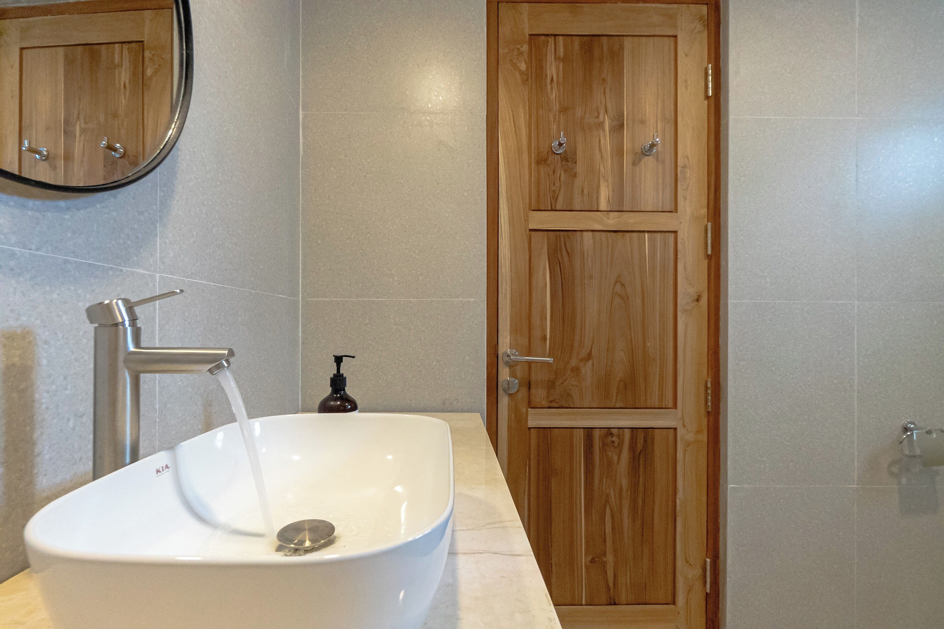 Un baño con lavamanos blanco, puerta de madera y paredes de baldosas.