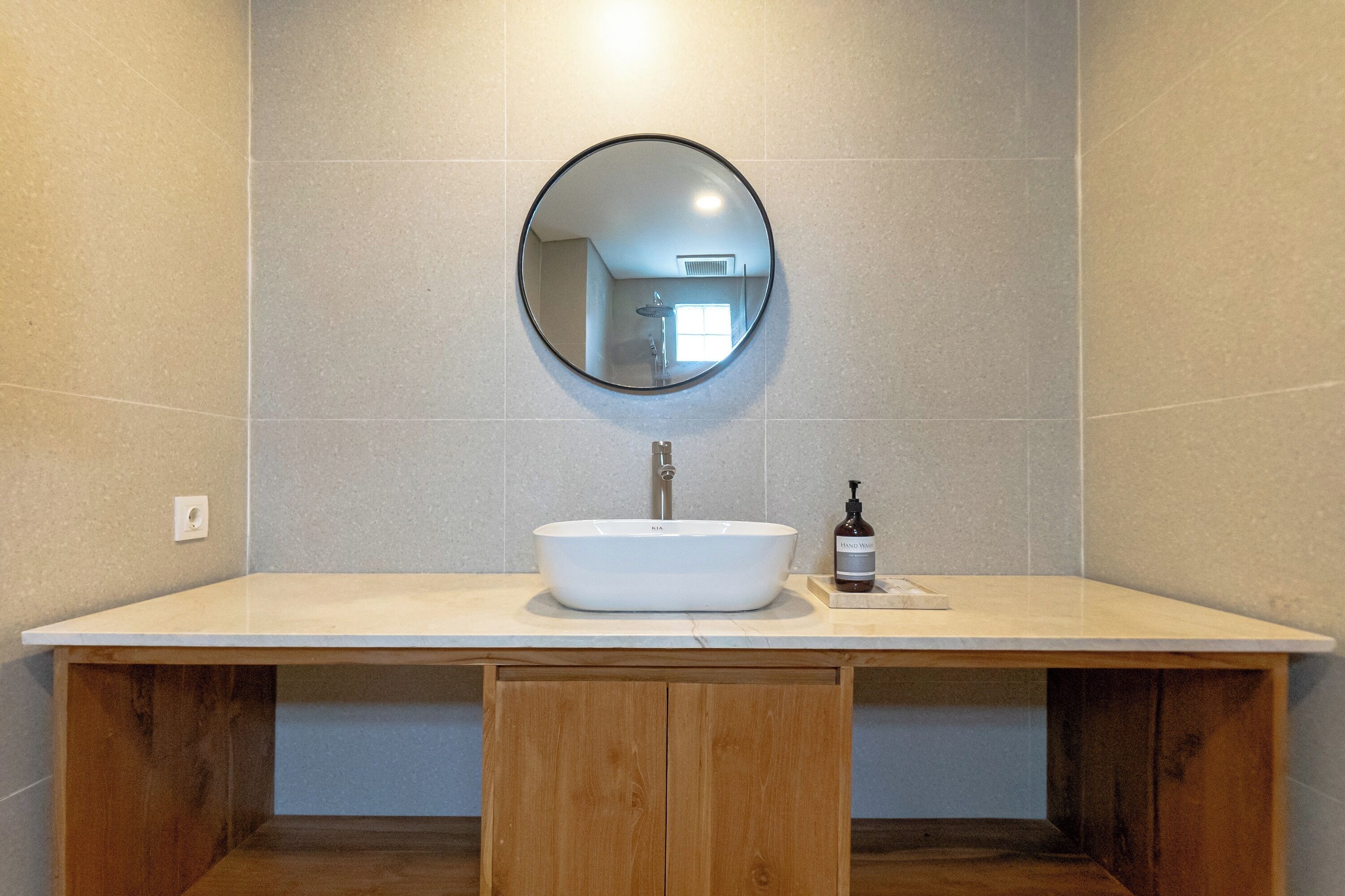 A bathroom with a white sink, a round mirror, and a bottle of hand soap on the counter.