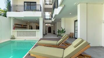 Zona de piscina interior moderna con sillones reclinables y vista al espacio interior.