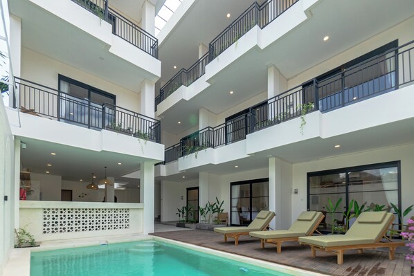 Ein Poolbereich im Innenbereich mit mehreren Ebenen, Liegestühlen, einem Pool und Balkonen mit Geländern.