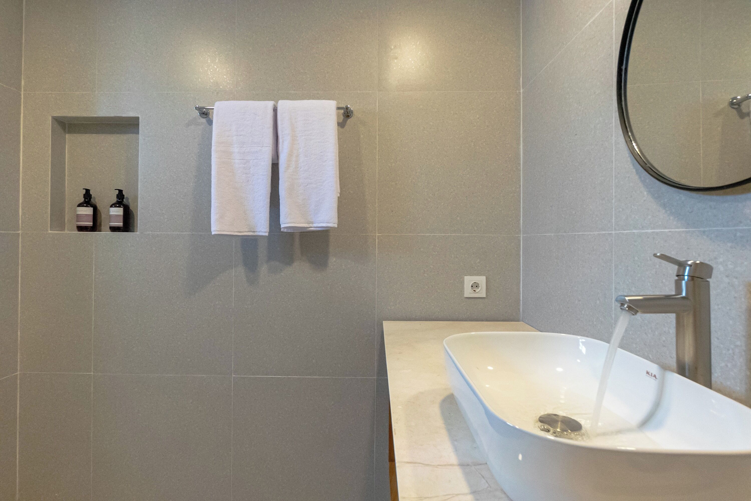 A modern bathroom with a large bathtub, a wall-mounted towel rack with two towels, and two bottles of hand soap.