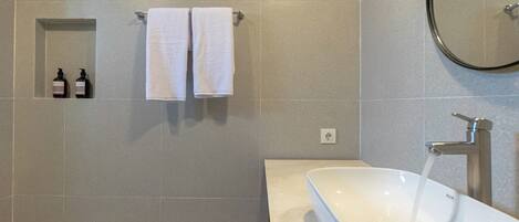A modern bathroom with a large bathtub, a wall-mounted towel rack with two towels, and two bottles of hand soap.