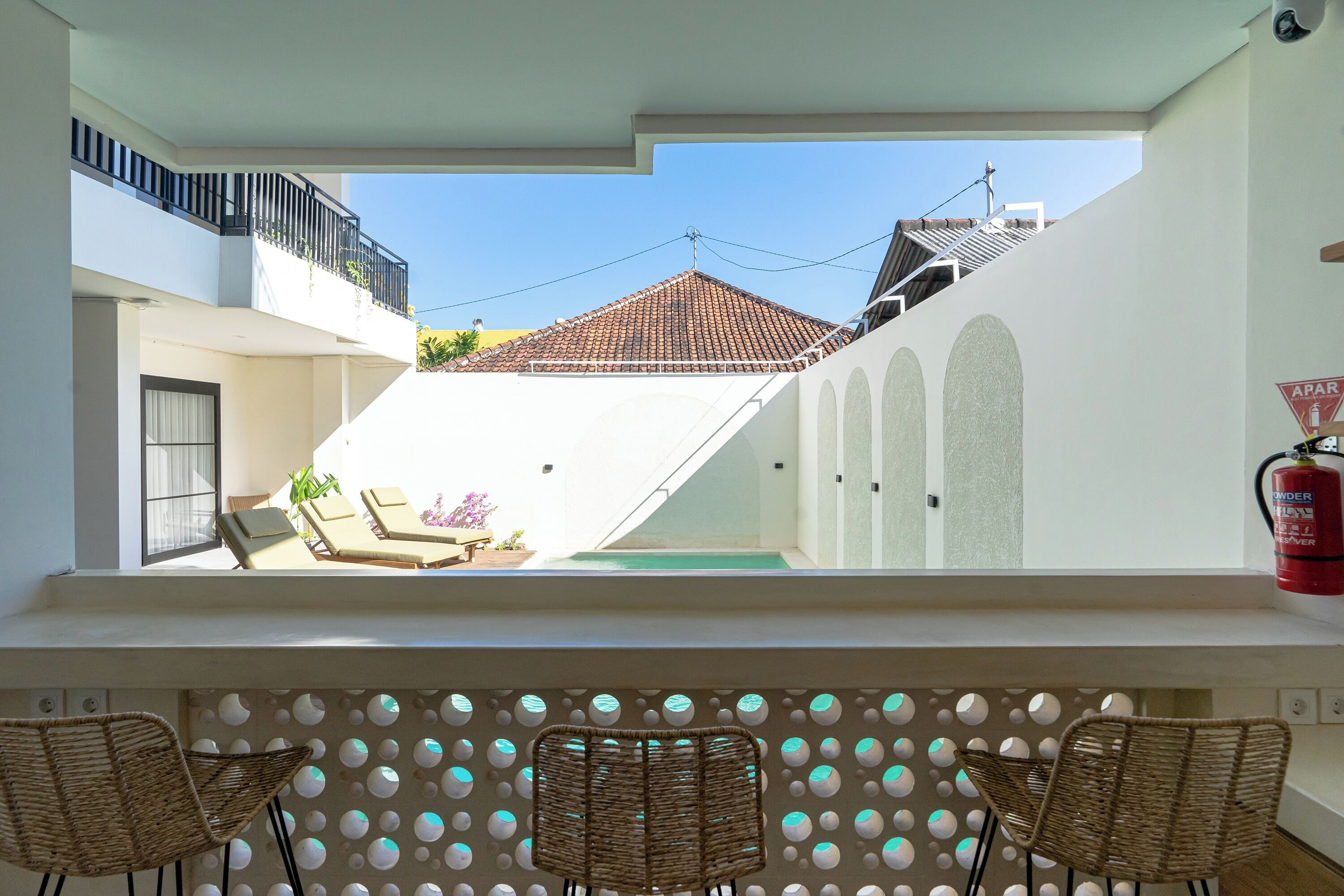 En balkon med fletstole, en pool og udsigt til en bygning med tegltag.