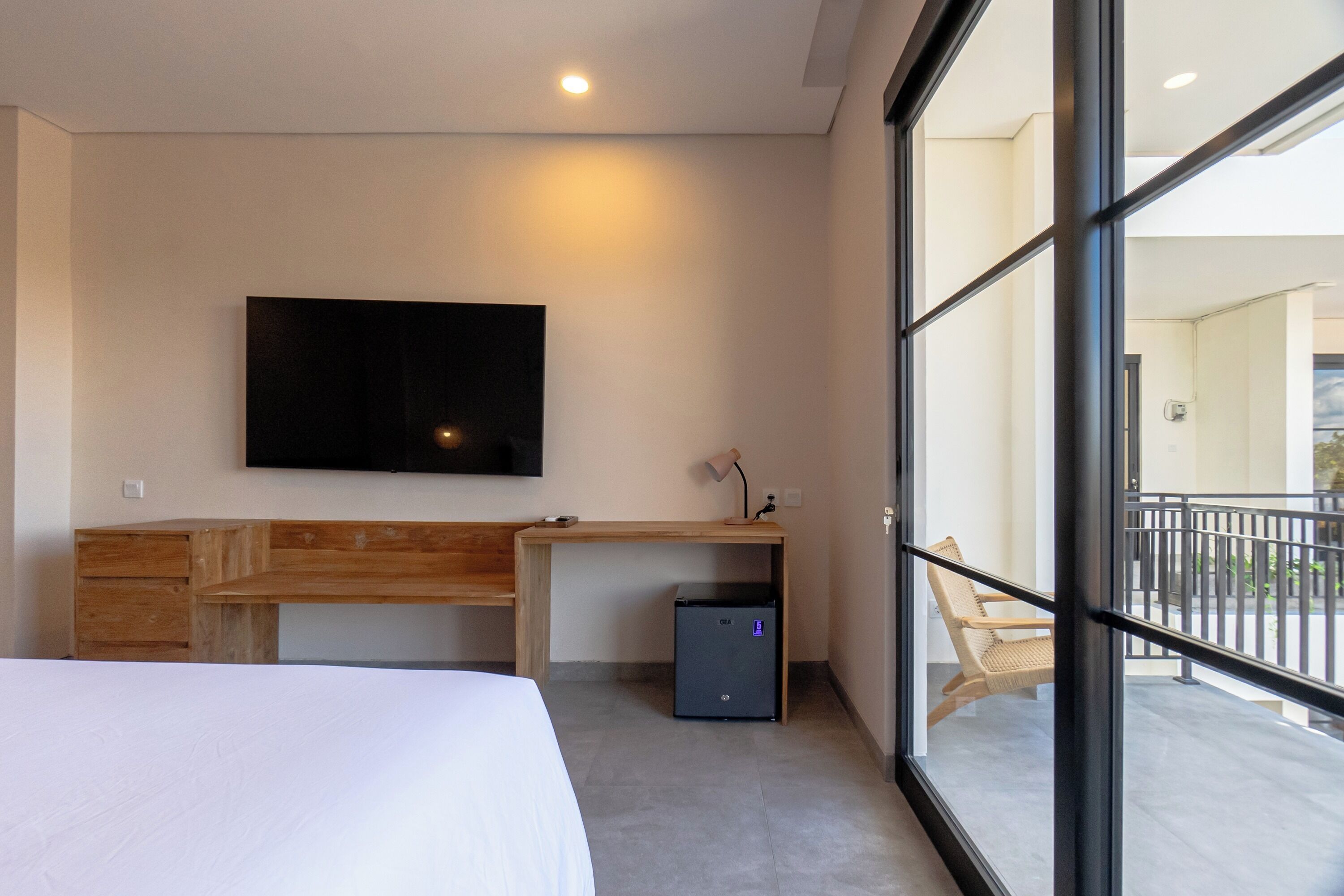 A hotel room with a bed, a desk, a television mounted on the wall, and a small refrigerator.