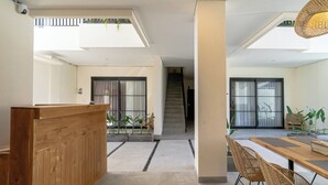 A spacious interior with a wooden reception desk, a dining area with wicker chairs, and a staircase leading to an upper level. - Kelaya Guesthouse (Denpasar)