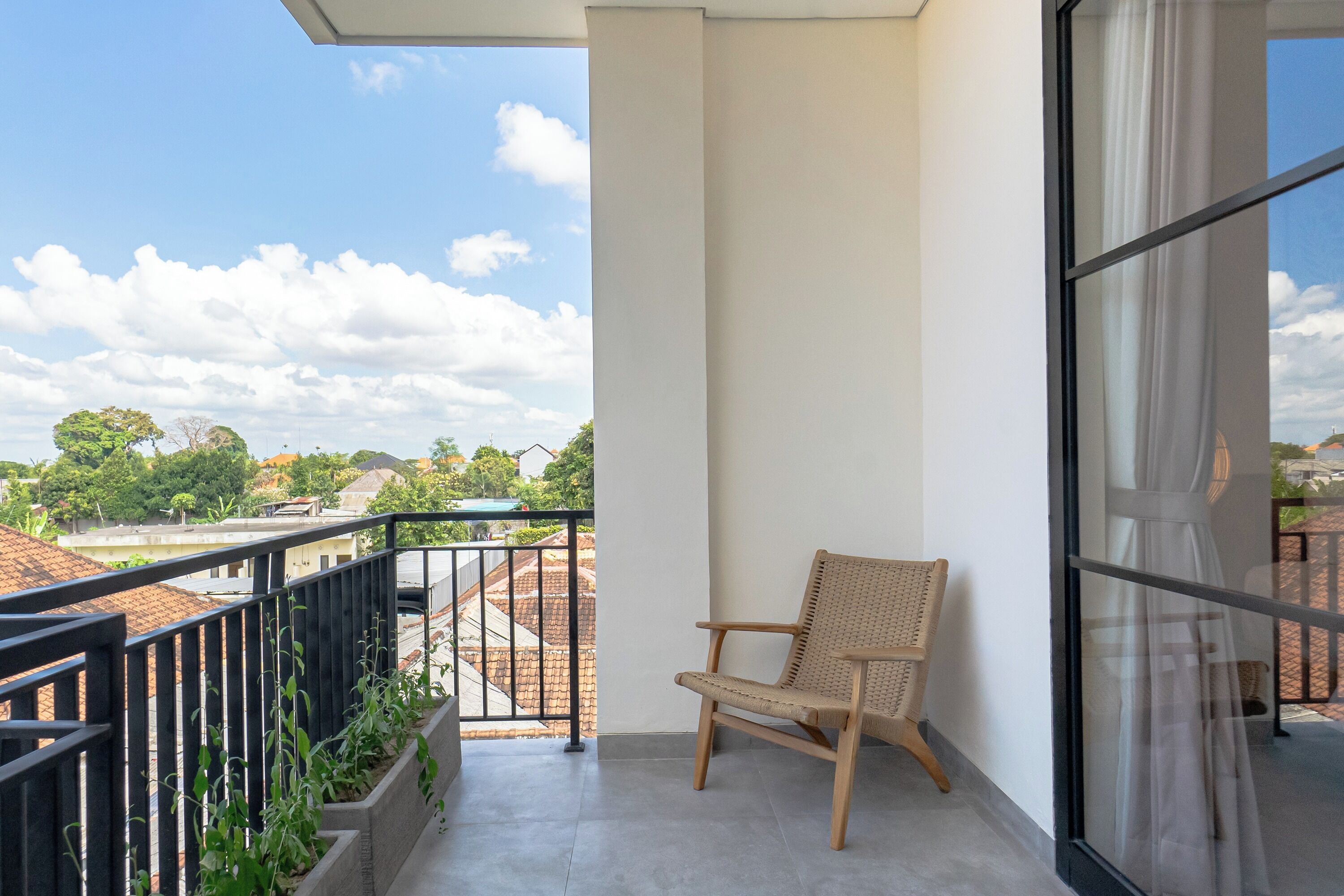 Un balcon avec un fauteuil en osier, une vue sur le paysage urbain et une porte vitrée.