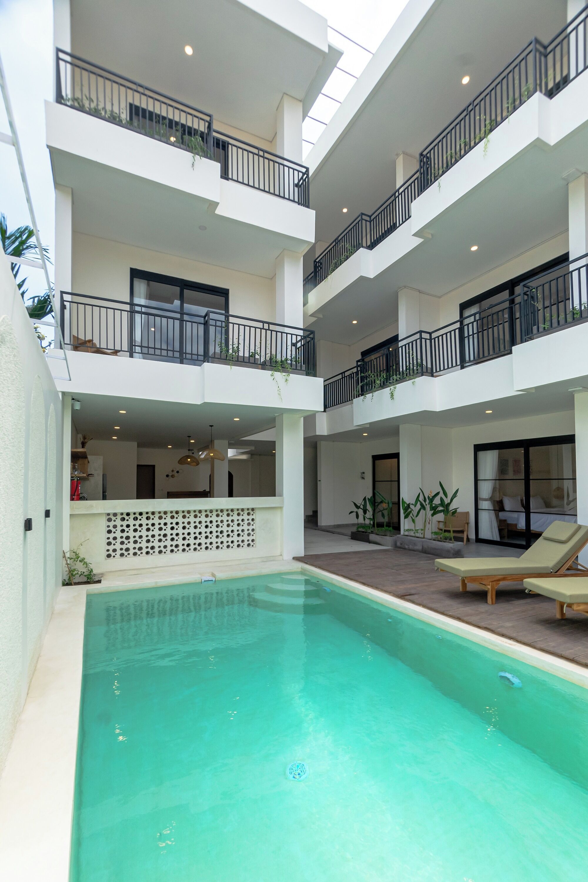 A multi-level indoor pool area with balconies, lounge chairs, and potted plants.