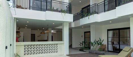 A multi-level indoor pool area with balconies, lounge chairs, and potted plants.