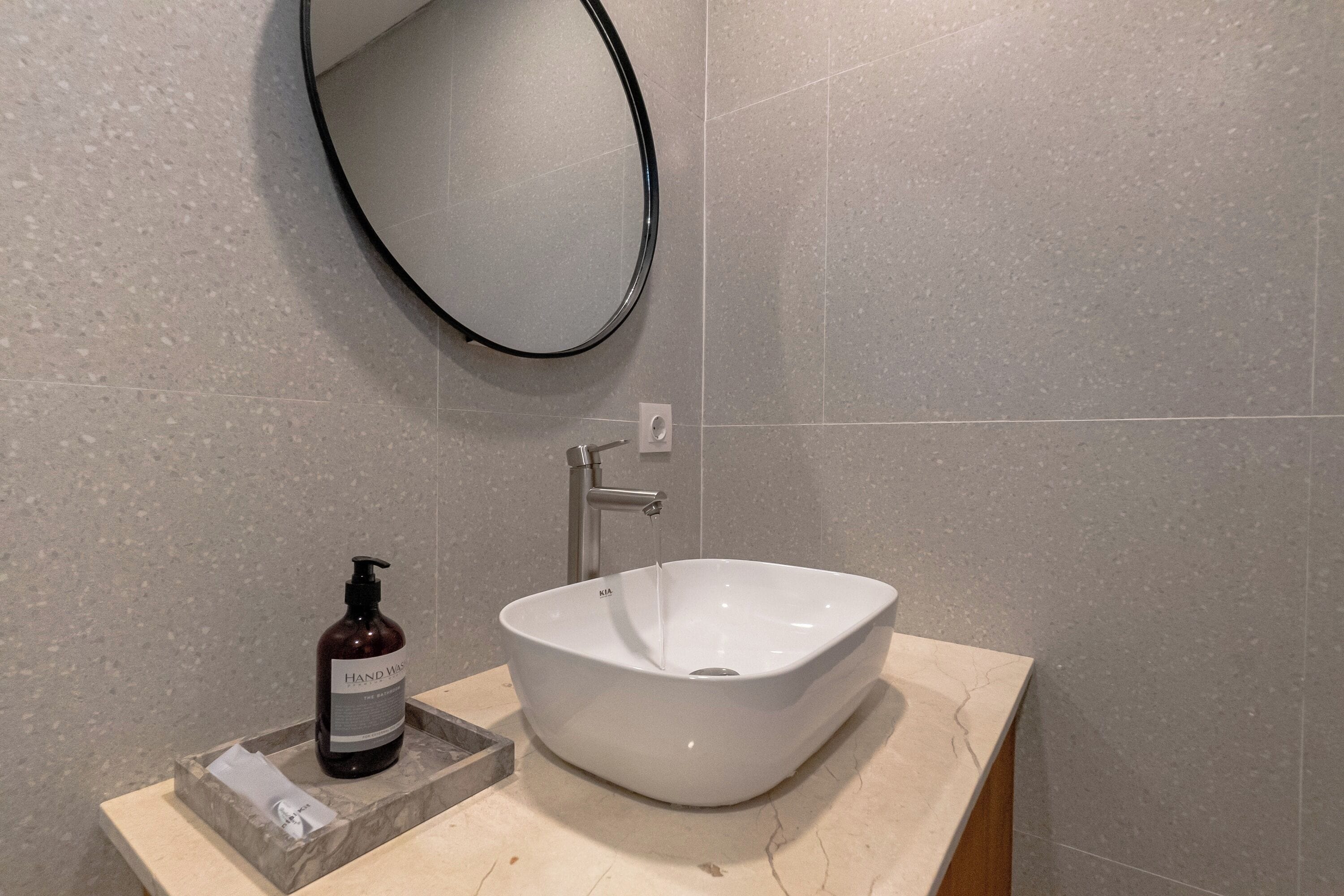 Une salle de bain avec un lavabo blanc, un miroir rond et un flacon de savon pour les mains.